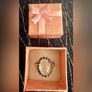 White moonstone ring surrounded by purple rhinestones in plated silver.